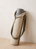 Oat Canvas Yoga Mat Bag with olive strap leaning against a limewashed wall