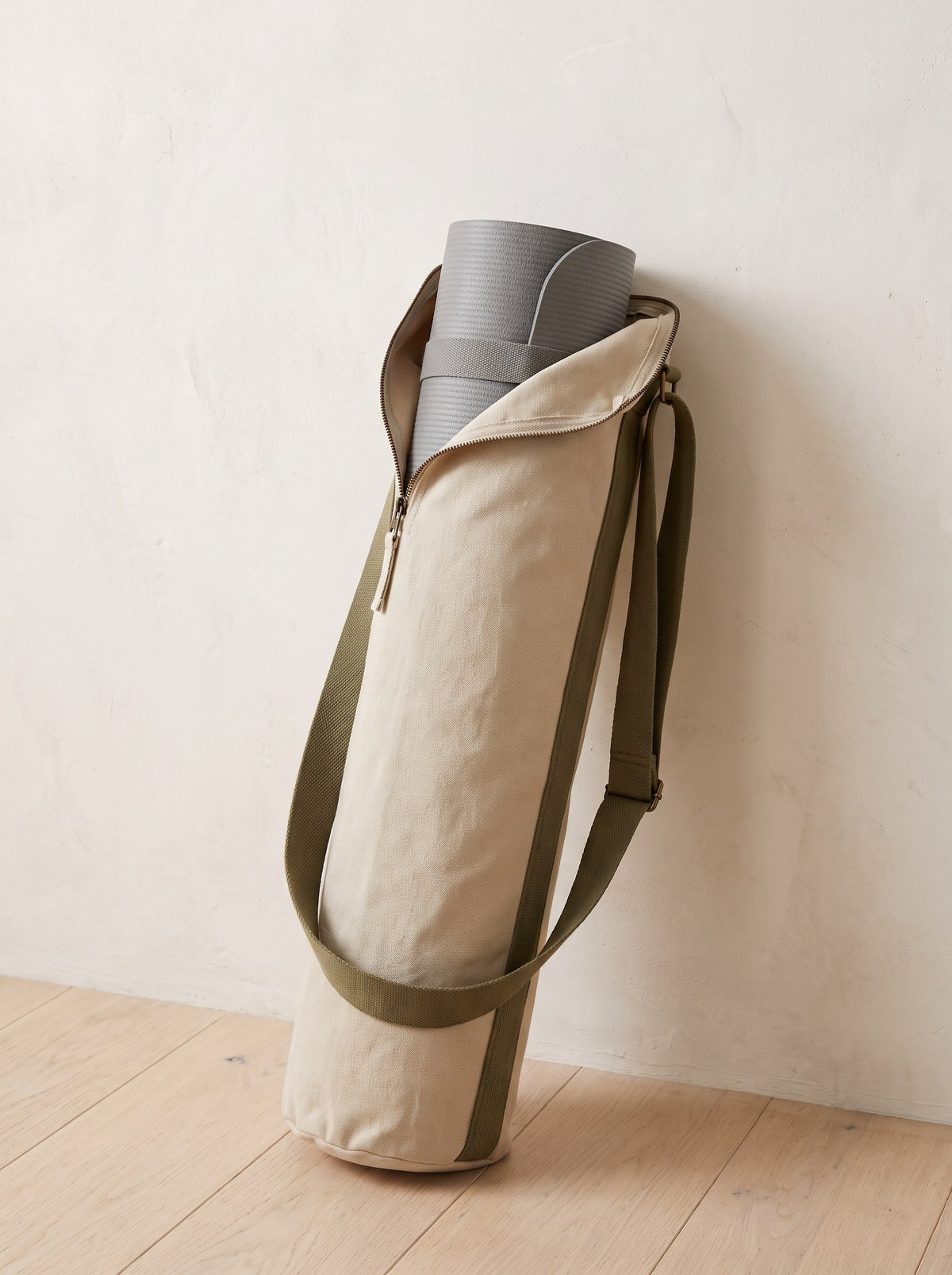 Oat Canvas Yoga Mat Bag with olive strap leaning against a limewashed wall