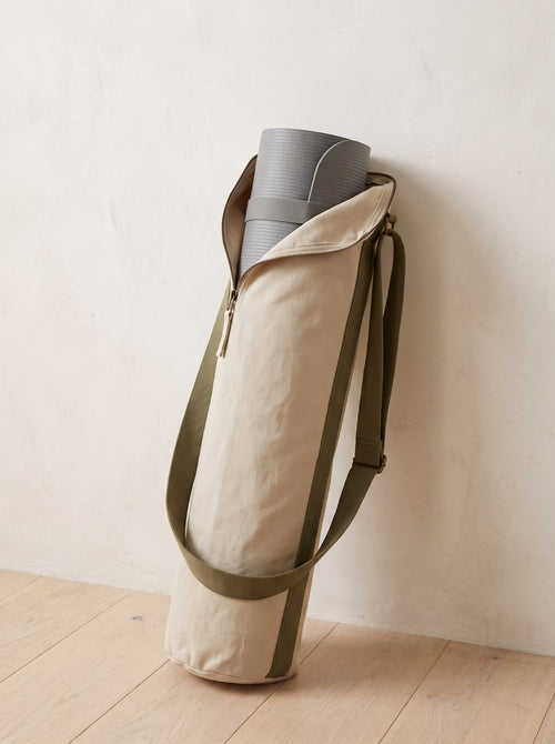 Oat Canvas Yoga Mat Bag with olive strap leaning against a limewashed wall
