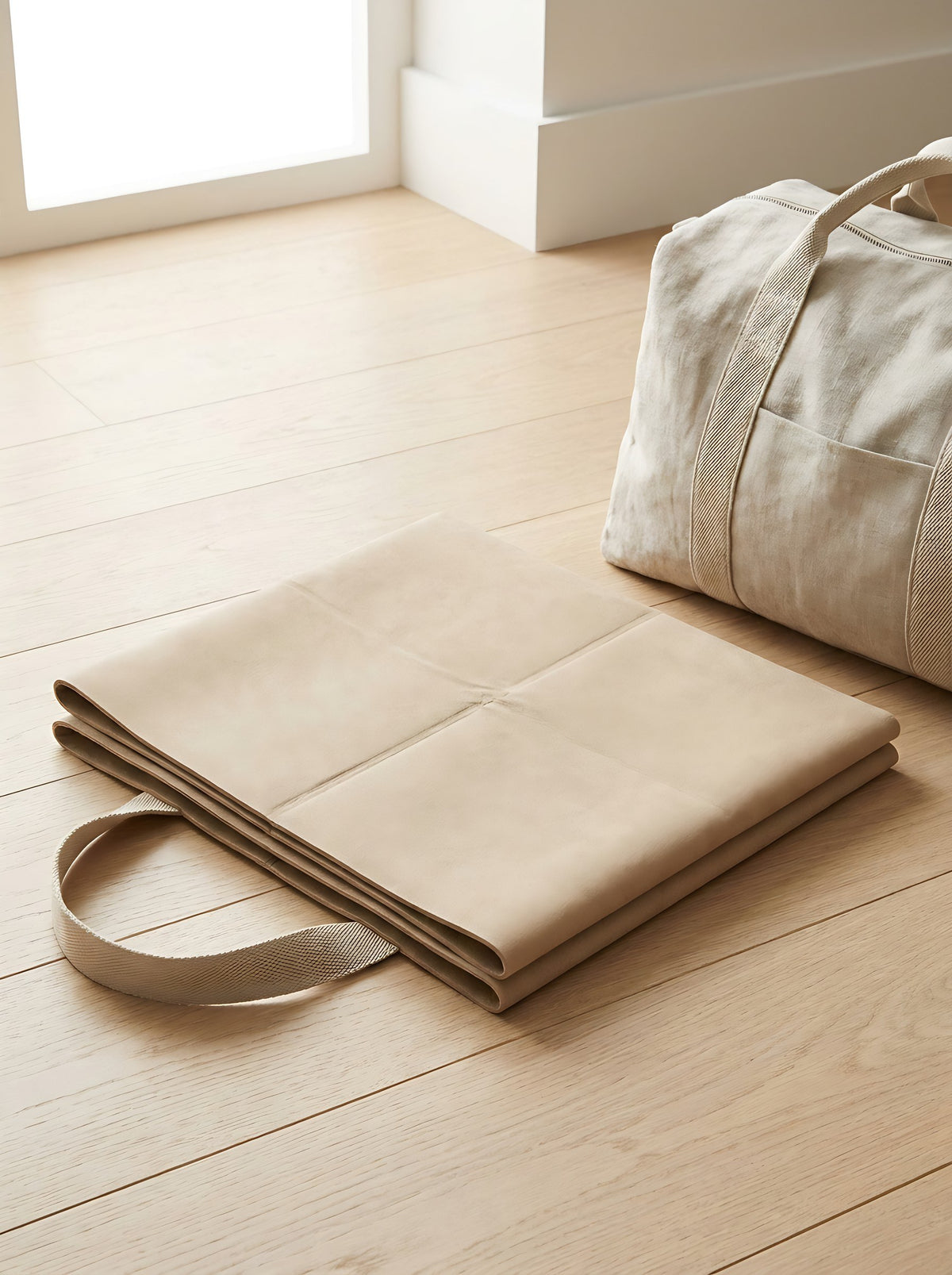 Sand Foldable Travel Yoga Mat folded flat beside a linen weekend bag