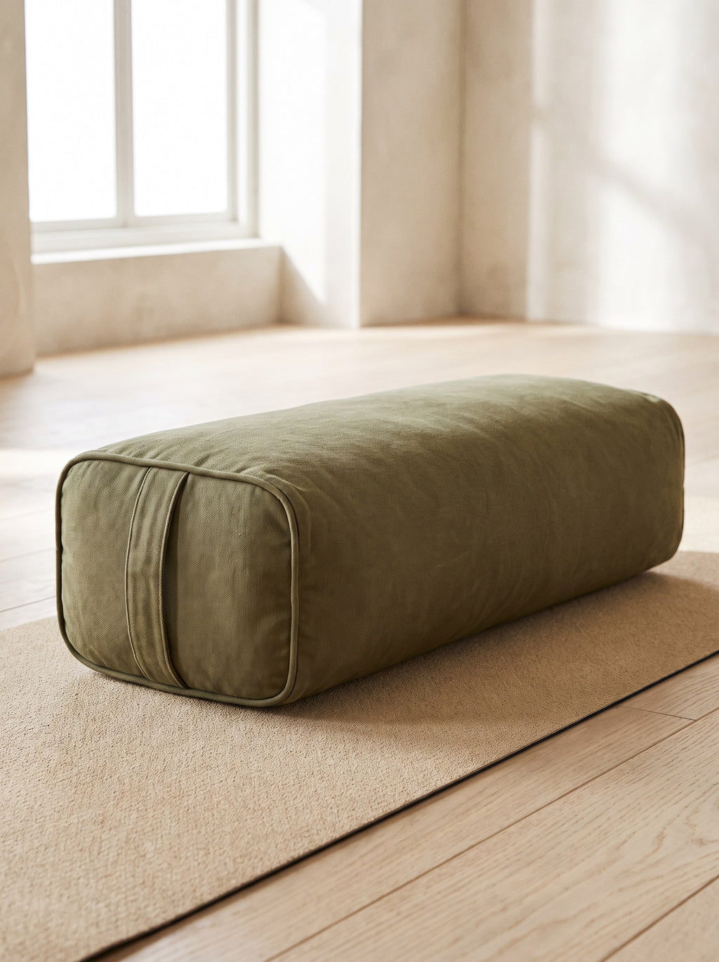 Olive Rectangular Yoga Bolster resting on a sand yoga mat in a bright studio