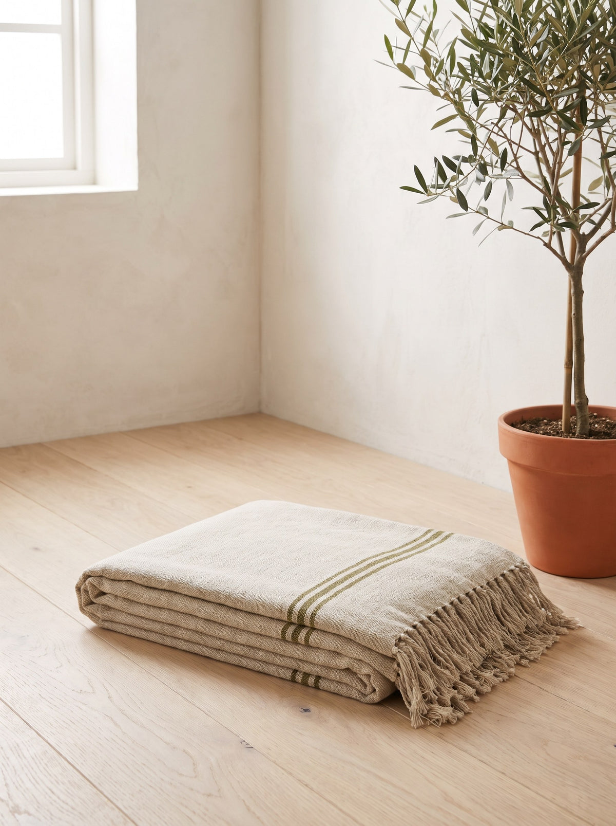 Folded oat Woven Cotton Yoga Blanket with olive stripes on an oak studio floor